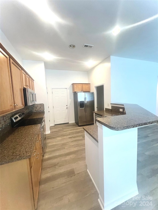 kitchen featuring stainless steel appliances, dark stone counters, decorative backsplash, kitchen peninsula, and light hardwood / wood-style flooring