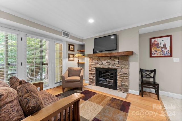 living room featuring light hardwood / wood-style floors, a stone fireplace, and crown molding