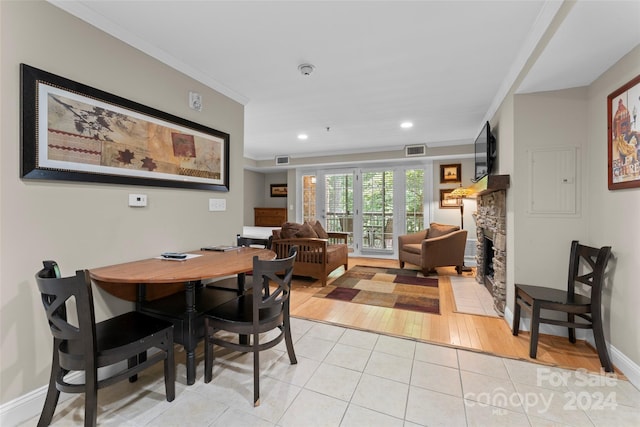 dining space featuring light wood-type flooring, a stone fireplace, and crown molding