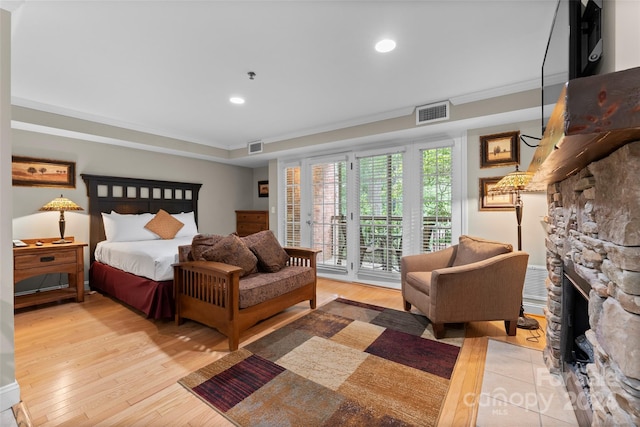 bedroom featuring a stone fireplace, ornamental molding, access to outside, and light hardwood / wood-style flooring