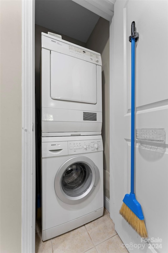 laundry area with light tile patterned flooring and stacked washing maching and dryer