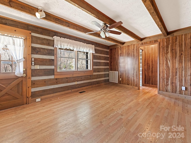 unfurnished living room featuring wooden walls, a textured ceiling, beam ceiling, and light hardwood / wood-style flooring