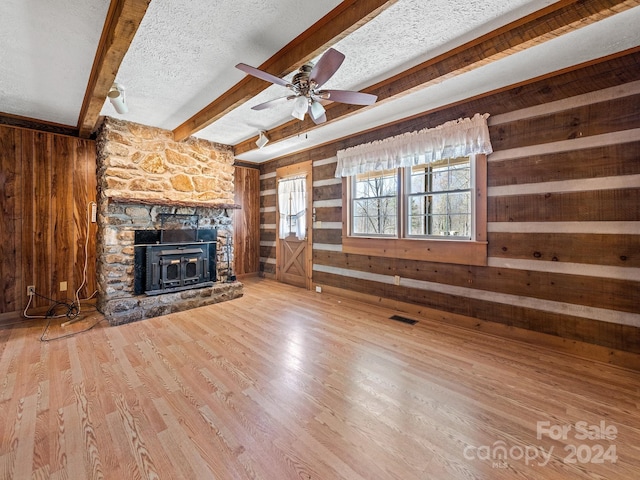 unfurnished living room with beam ceiling, wooden walls, wood-type flooring, a fireplace, and a textured ceiling