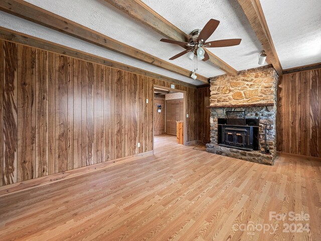 unfurnished living room with beam ceiling, a textured ceiling, a fireplace, and light wood-type flooring