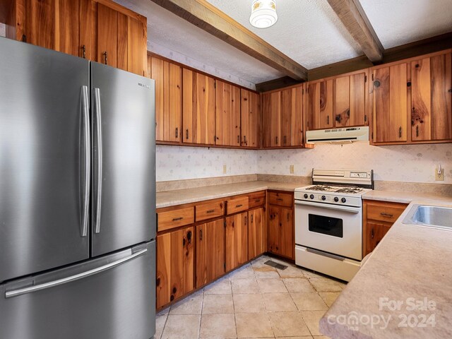 kitchen with white range with gas cooktop, stainless steel fridge, beam ceiling, a textured ceiling, and light tile floors