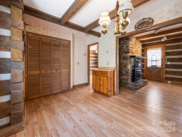 unfurnished living room with an inviting chandelier, a fireplace, beam ceiling, and light hardwood / wood-style flooring