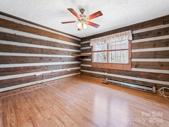 unfurnished room with a textured ceiling, hardwood / wood-style flooring, wood walls, baseboard heating, and ceiling fan