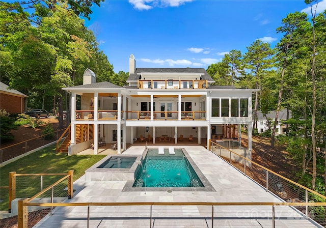 rear view of property featuring a balcony, ceiling fan, a swimming pool with hot tub, a patio area, and a yard