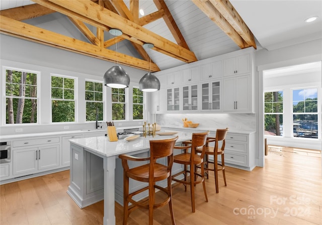 kitchen featuring beam ceiling, backsplash, decorative light fixtures, a center island with sink, and white cabinets