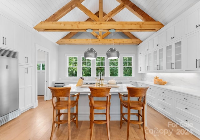 kitchen featuring built in fridge, beamed ceiling, white cabinetry, a breakfast bar area, and an island with sink