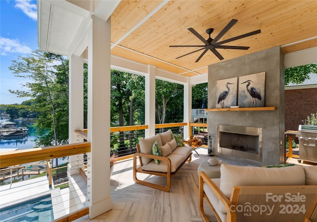 sunroom featuring ceiling fan, a large fireplace, a water view, and wooden ceiling