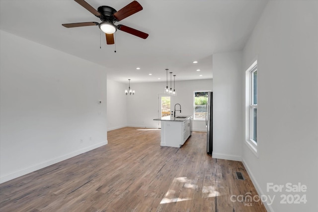 unfurnished living room featuring ceiling fan with notable chandelier, light wood-type flooring, and sink