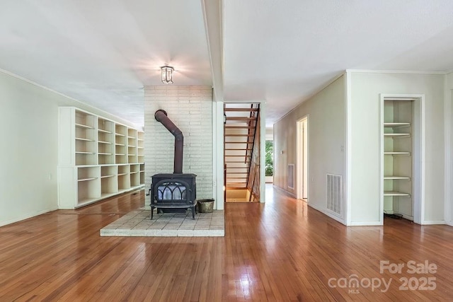 unfurnished living room with hardwood / wood-style floors, built in features, a wood stove, and crown molding