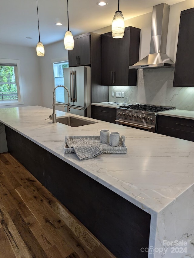 kitchen with backsplash, premium appliances, hanging light fixtures, light stone counters, and wall chimney range hood