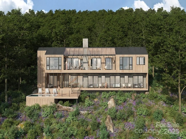 rear view of property with a chimney, a deck, and a forest view