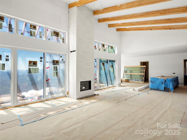 unfurnished living room featuring beamed ceiling, a high ceiling, and a fireplace