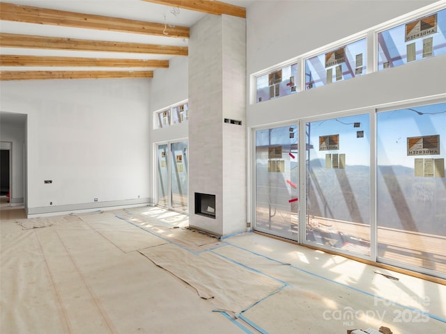 unfurnished living room featuring baseboards, a high ceiling, beam ceiling, and a large fireplace