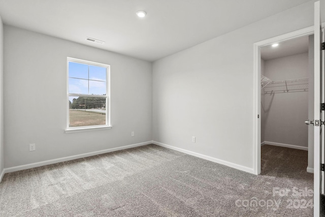 unfurnished bedroom featuring carpet flooring, a walk in closet, and a closet