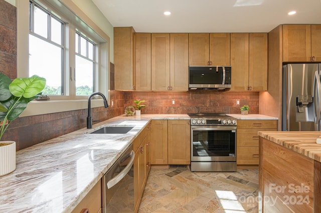 kitchen featuring decorative backsplash, stainless steel appliances, light stone counters, and sink