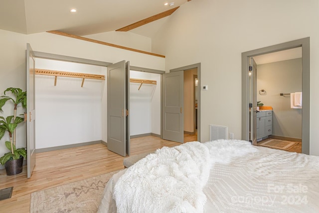 bedroom featuring light wood-type flooring, beam ceiling, connected bathroom, and high vaulted ceiling