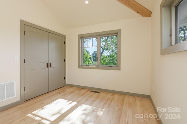 unfurnished bedroom with vaulted ceiling with beams, a closet, and light hardwood / wood-style floors