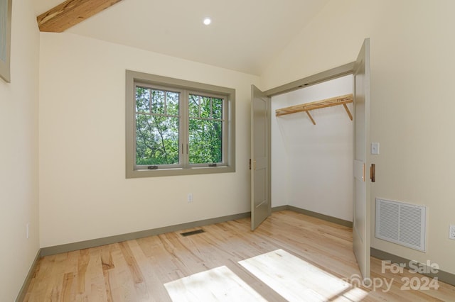 unfurnished bedroom with light wood-type flooring, lofted ceiling with beams, and a closet