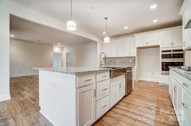 kitchen with stainless steel double oven, light stone countertops, hanging light fixtures, and a kitchen island with sink