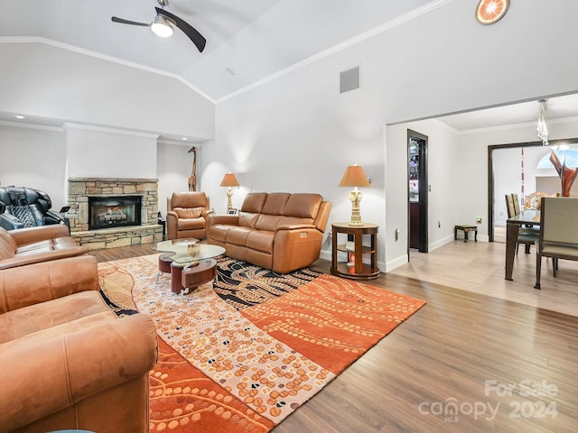 living room with a stone fireplace, ceiling fan, high vaulted ceiling, ornamental molding, and light hardwood / wood-style flooring