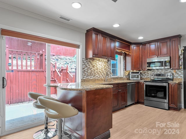 kitchen featuring light stone countertops, kitchen peninsula, appliances with stainless steel finishes, and a kitchen breakfast bar