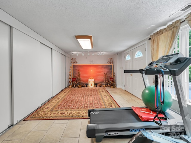 workout area featuring a textured ceiling, light tile patterned floors, and track lighting