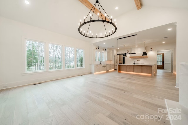 unfurnished living room with lofted ceiling with beams, light wood-type flooring, and a chandelier