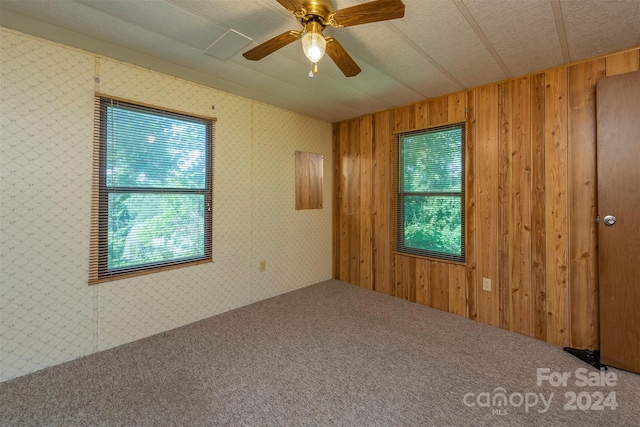 carpeted empty room with ceiling fan and wooden walls