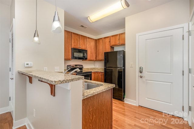 kitchen featuring a kitchen breakfast bar, light hardwood / wood-style flooring, kitchen peninsula, decorative light fixtures, and black appliances