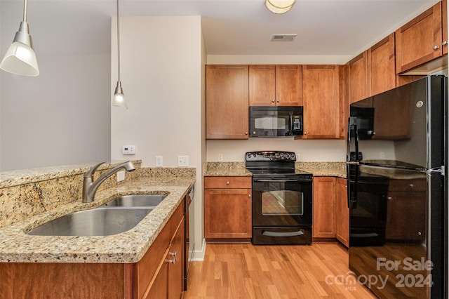 kitchen featuring black appliances, sink, light stone countertops, decorative light fixtures, and light hardwood / wood-style floors