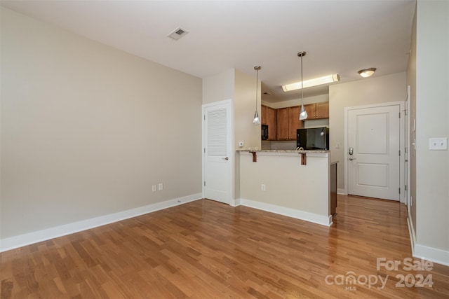 kitchen featuring kitchen peninsula, light hardwood / wood-style floors, black refrigerator, and hanging light fixtures