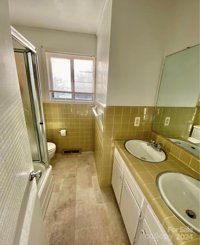 full bathroom with shower / bath combination with glass door, vanity, toilet, and tile walls