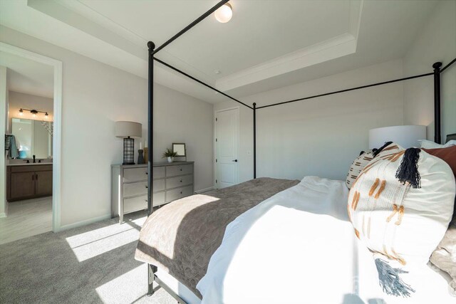 bedroom featuring connected bathroom, light colored carpet, a raised ceiling, and sink