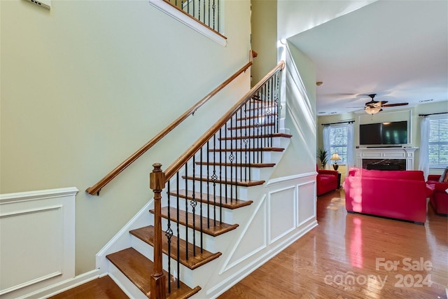 staircase featuring a premium fireplace, hardwood / wood-style floors, and ceiling fan