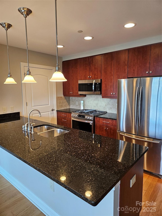 kitchen featuring sink, dark stone countertops, stainless steel appliances, and pendant lighting