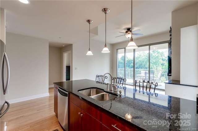 kitchen with sink, dark stone countertops, appliances with stainless steel finishes, pendant lighting, and light hardwood / wood-style floors