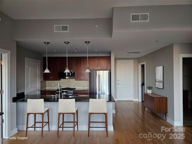 kitchen with tasteful backsplash, appliances with stainless steel finishes, a kitchen breakfast bar, pendant lighting, and light hardwood / wood-style floors