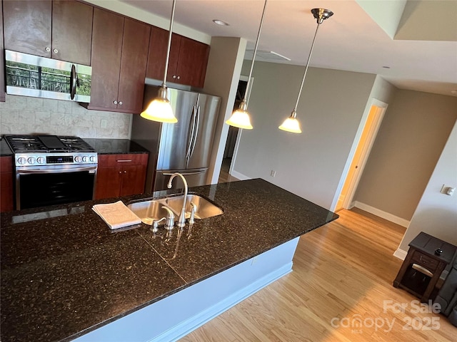 kitchen with sink, appliances with stainless steel finishes, dark stone countertops, hanging light fixtures, and light wood-type flooring