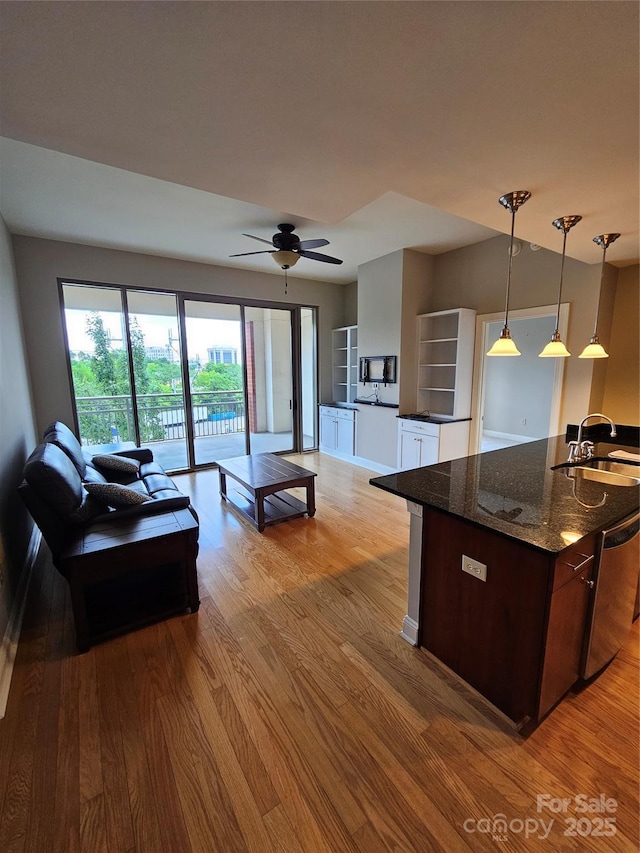 kitchen featuring decorative light fixtures, dishwasher, sink, dark stone counters, and light wood-type flooring