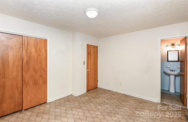 unfurnished bedroom featuring connected bathroom, a closet, a textured ceiling, and sink