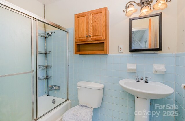 bathroom featuring toilet, combined bath / shower with glass door, and tile walls