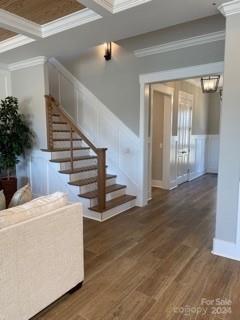 stairway featuring hardwood / wood-style floors, ornamental molding, coffered ceiling, and beamed ceiling