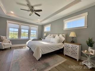 bedroom with ceiling fan, a tray ceiling, and dark hardwood / wood-style flooring