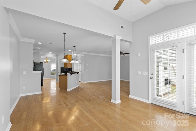 unfurnished living room featuring light hardwood / wood-style floors, ornate columns, ornamental molding, and vaulted ceiling