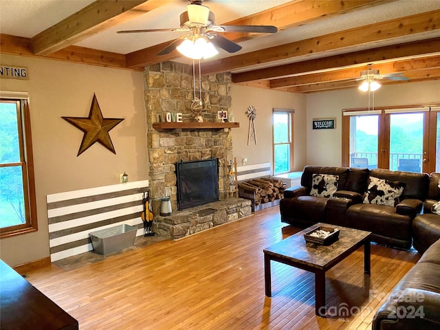 living room featuring hardwood / wood-style floors, ceiling fan, a stone fireplace, and beamed ceiling