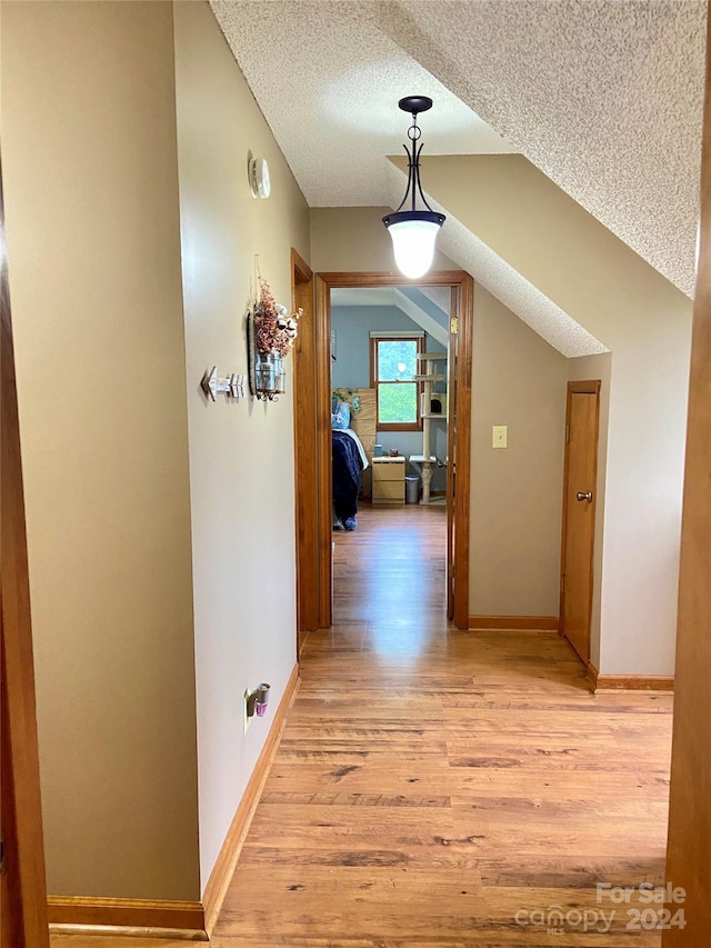 hallway featuring vaulted ceiling, a textured ceiling, and light hardwood / wood-style flooring